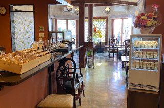 暖色系の照明に包まれたカフェの店内。左手には焼き菓子が並ぶカウンター、右手には瓶入りのスイーツが陳列された冷蔵ケースがあり、奥にはステンドグラスのある客席が見える落ち着いた空間。